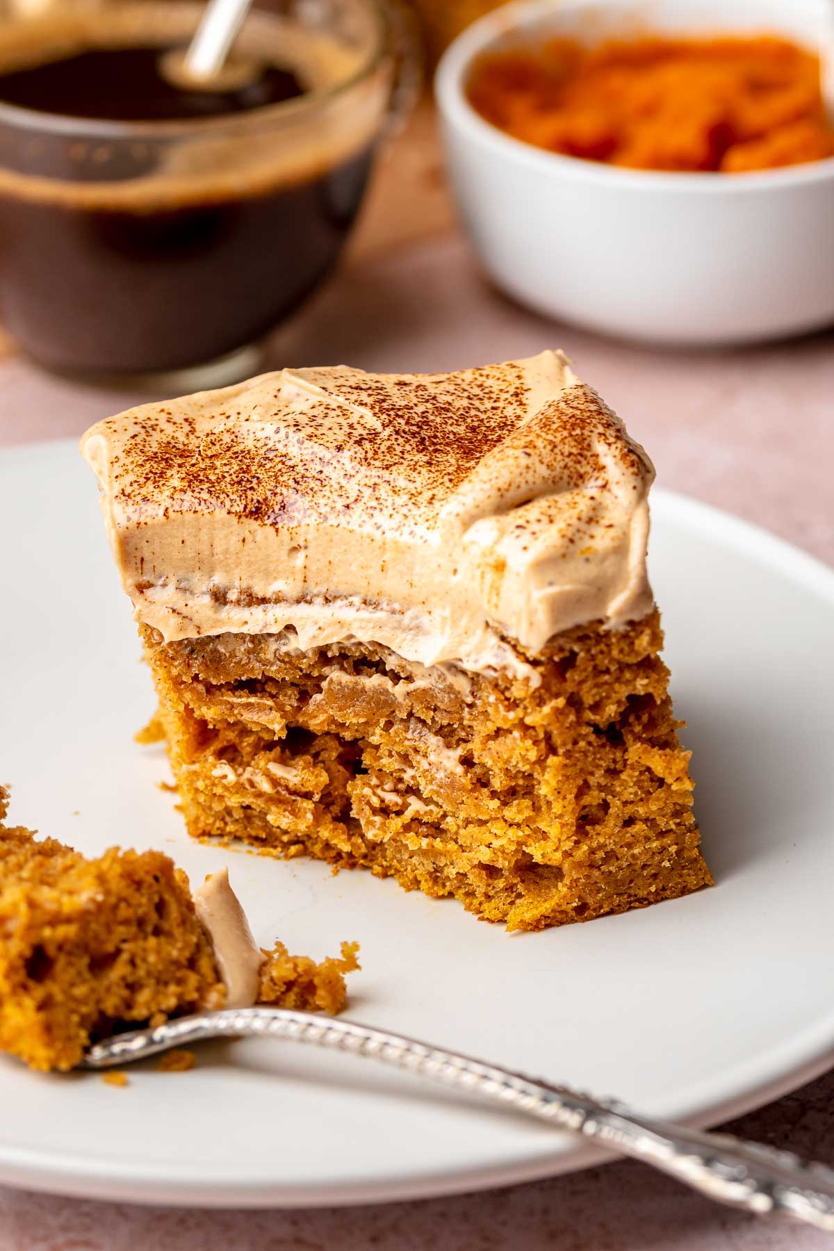 A square slice of pumpkin spice latte cake on a plate with a fork. A bite is removed.