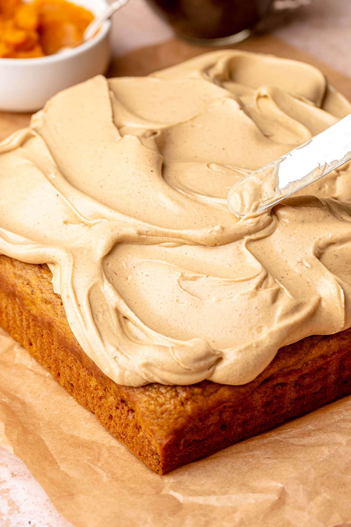 A spatula spreads espresso frosting onto a pumpkin cake.