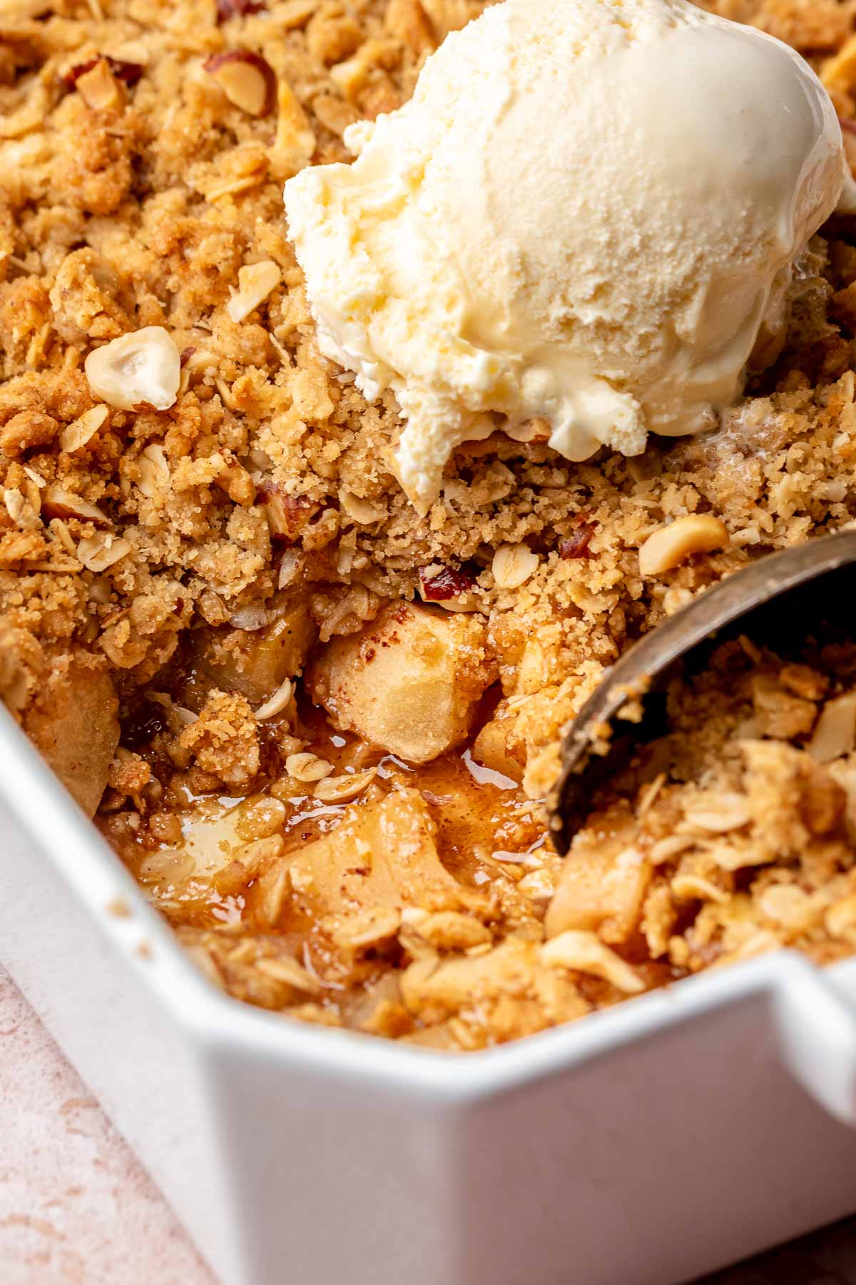 A spoon scoops toffee apple crumble from a casserole dish.
