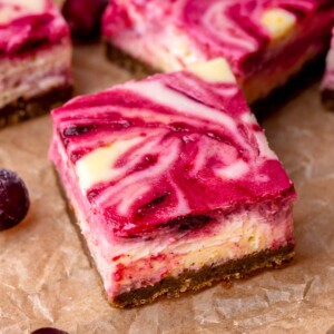 A square of cranberry cheesecake bar cut on parchment paper.
