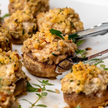Tongs move around a boursin stuffed mushroom on a platter.