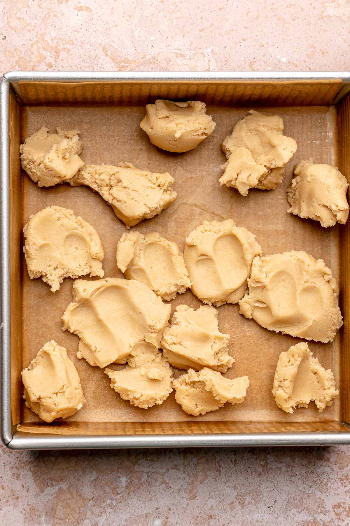 Dollops of shortbread dough in a prepared square pan.