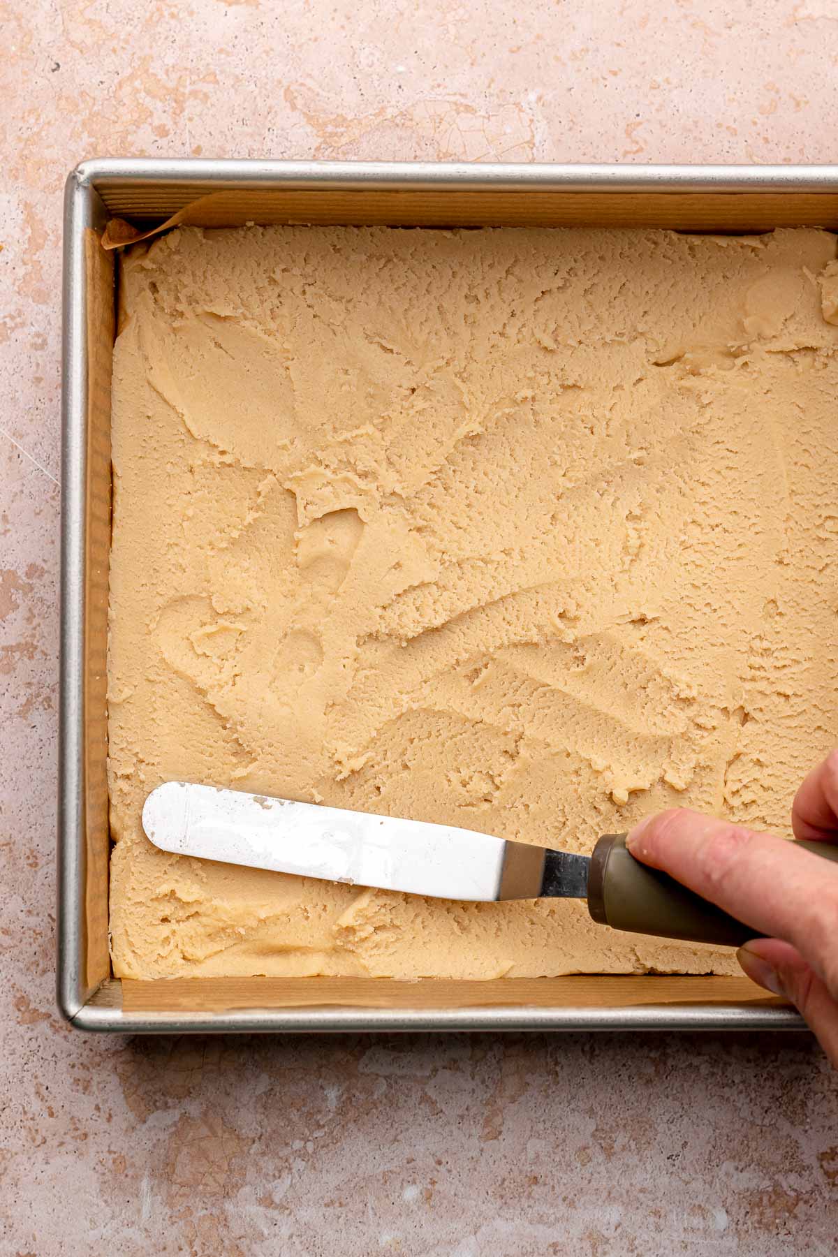 An offset spatula spreads shortbread dough into a pan.
