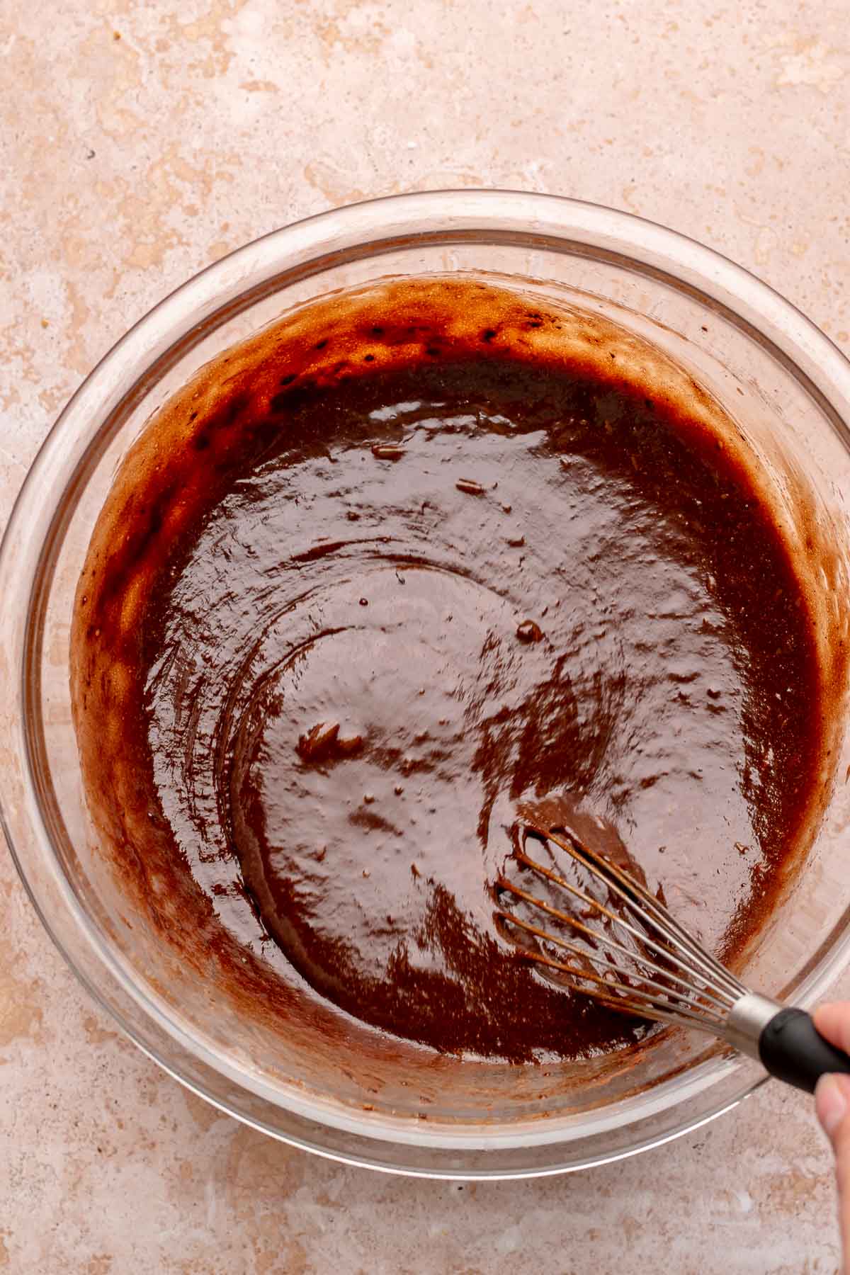 A whisk mixes chocolate pecan pie batter in a bowl.