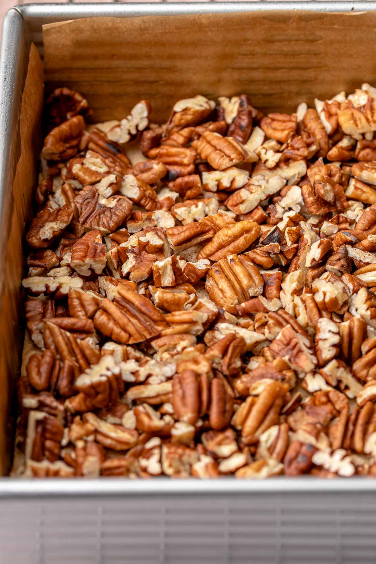 Chopped pecans scattered onto shortbread dough in a pan.