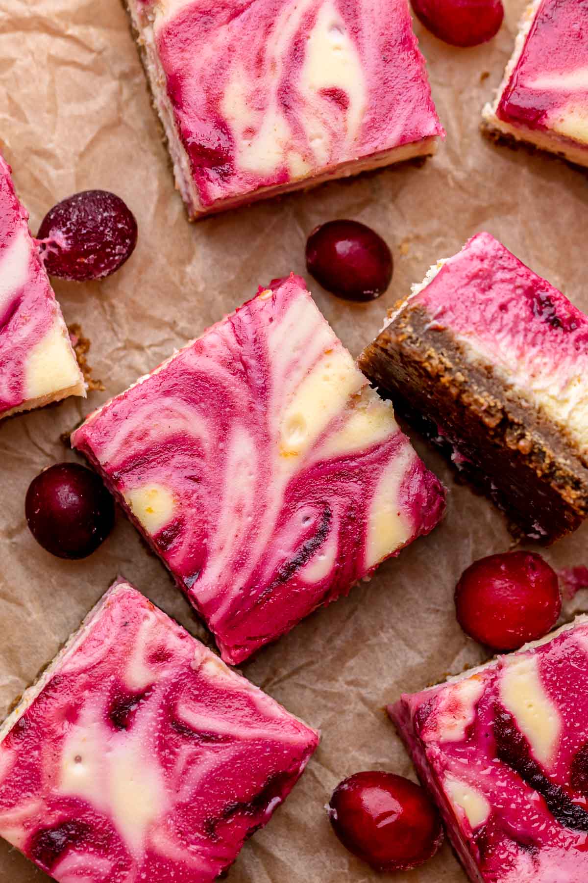 Cut cranberry cheesecake bars with cranberries scattered around.