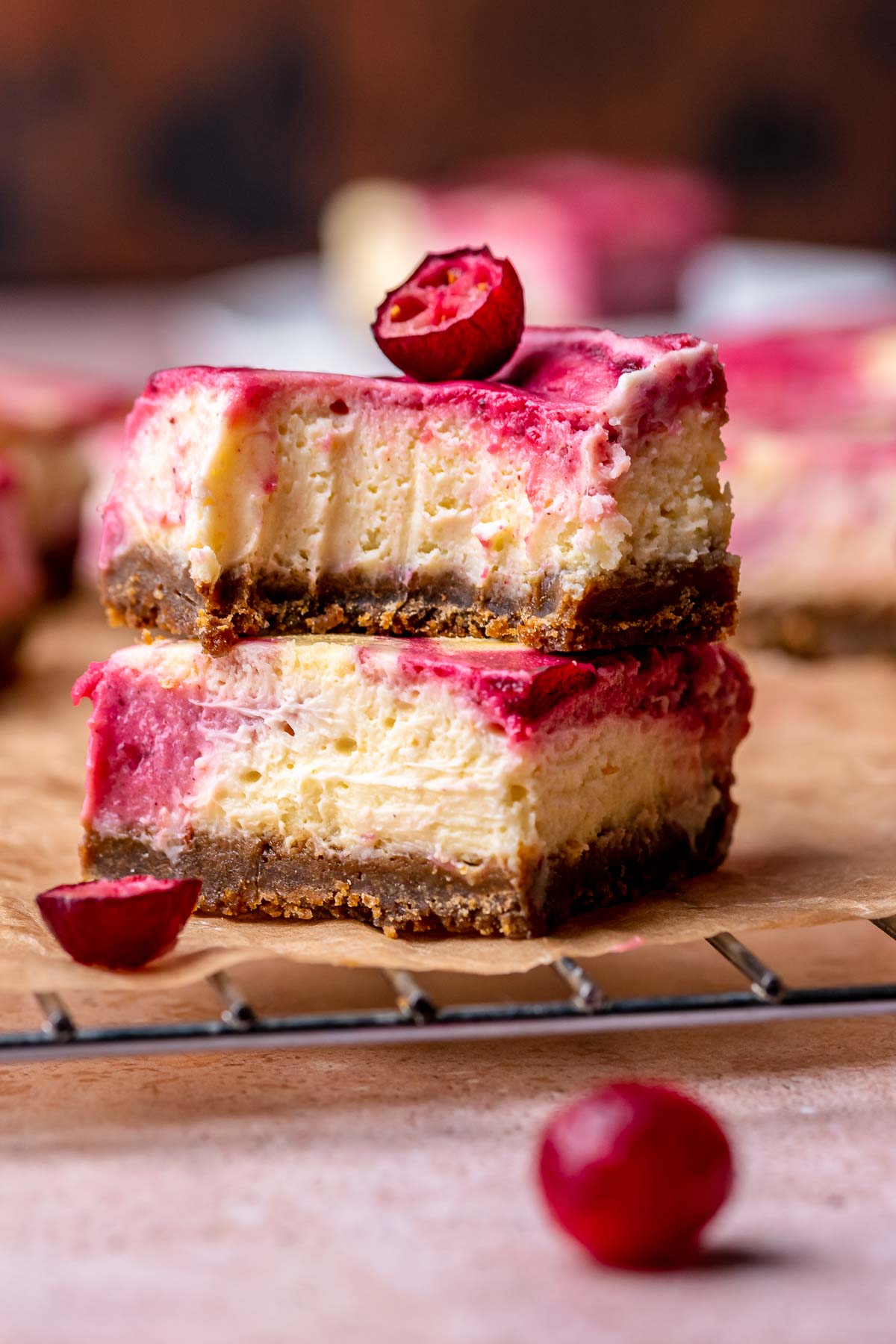 Two pieces of cranberry cheesecake bars stacked on top of each other. The top bar has a bite removed.