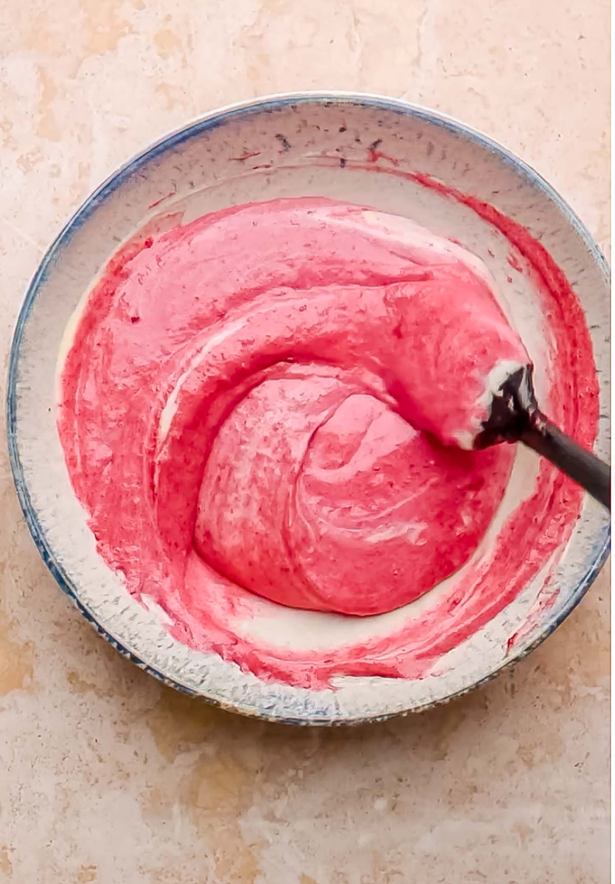 Cranberry puree and cheesecake batter get mixed with a spatula.