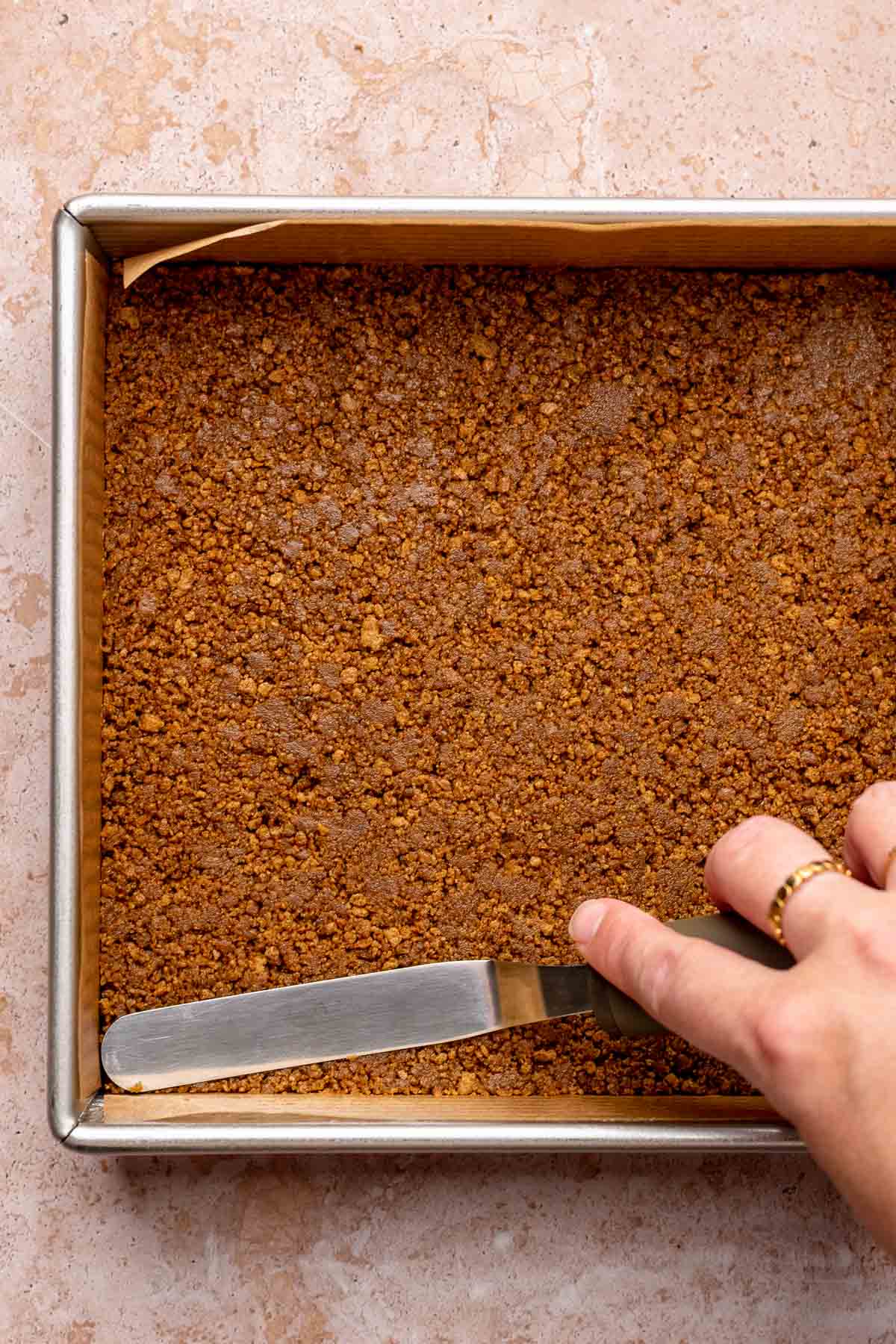 An offset spatula spreads gingersnap crust into a square pan.