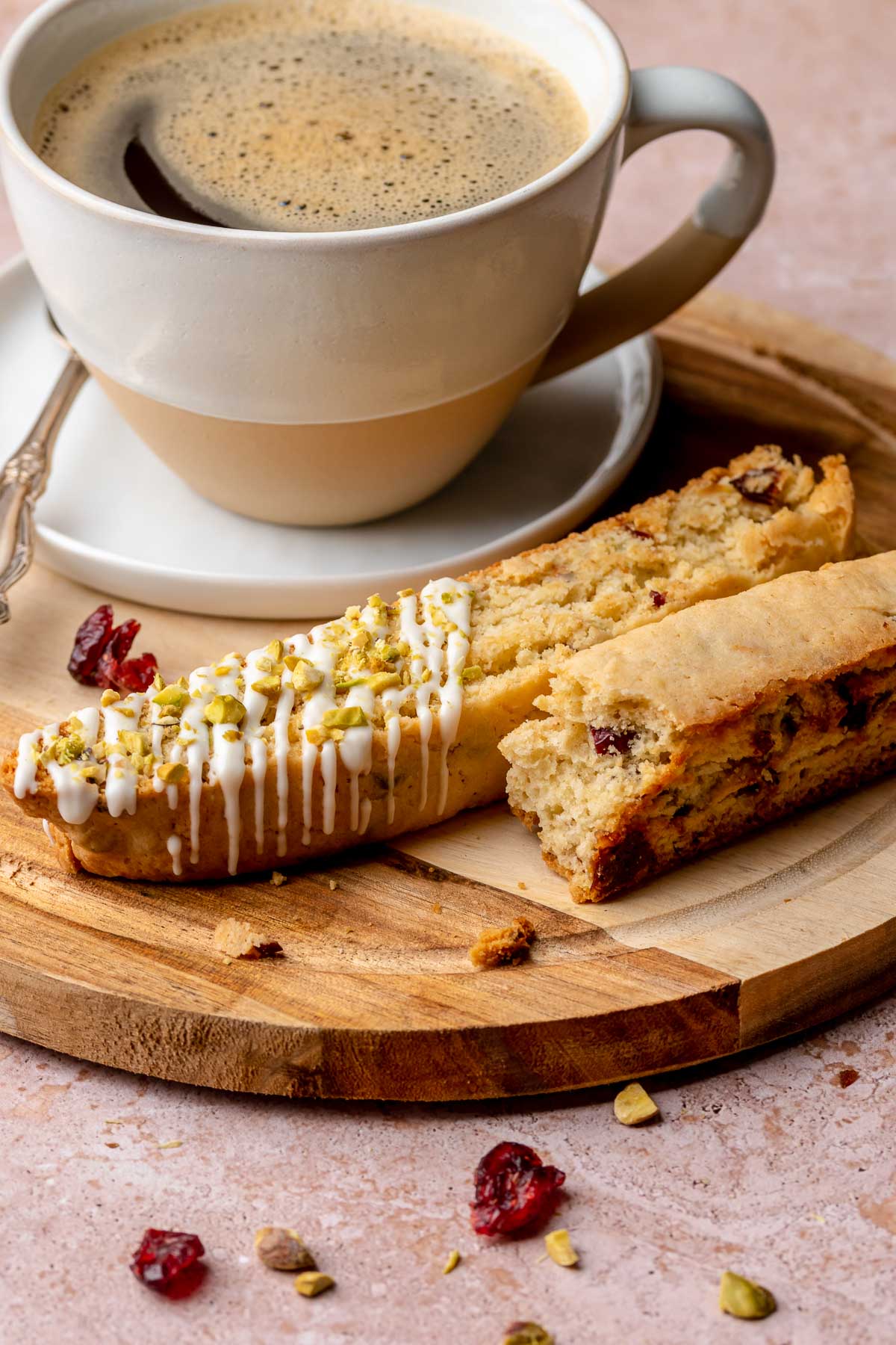Pistachio biscotti pieces on a plate with a coffee cup.