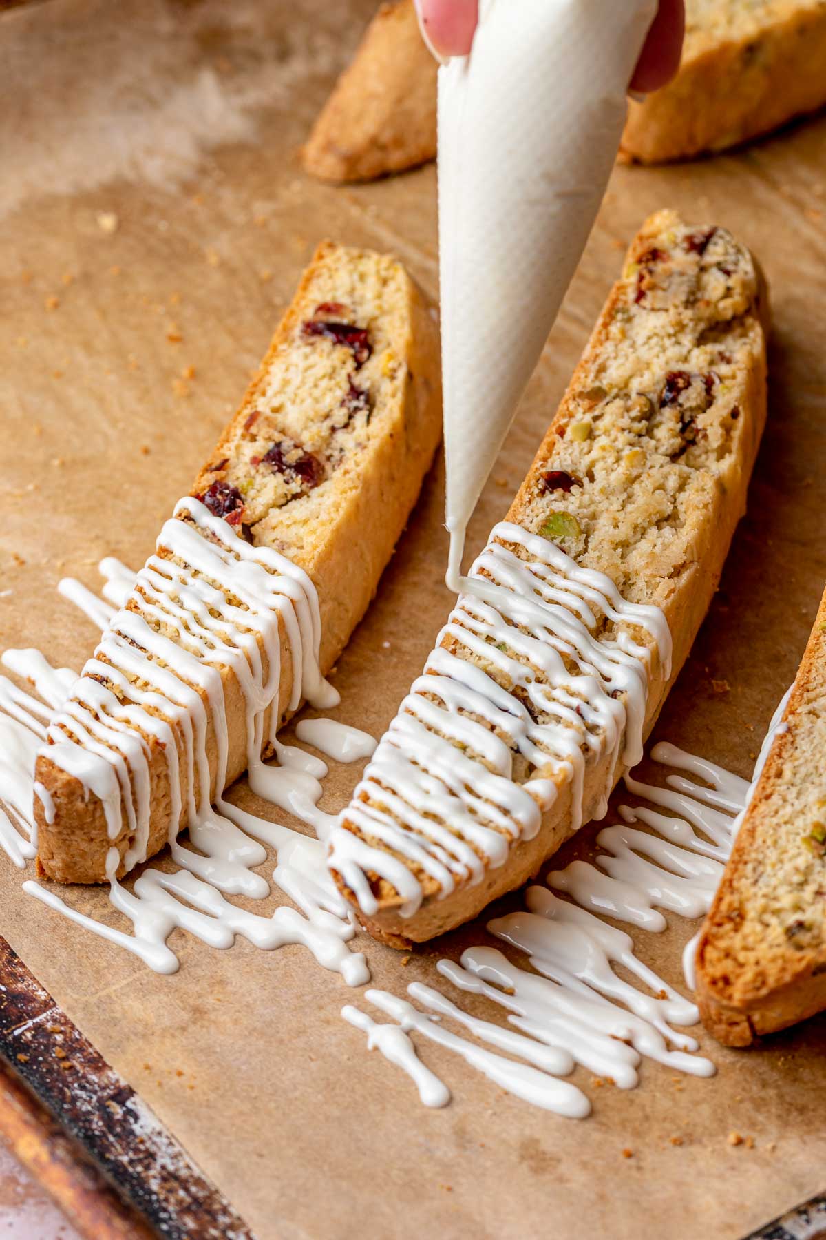 A piping bag drizzles white chocolate onto baked cranberry pistachio biscotti.