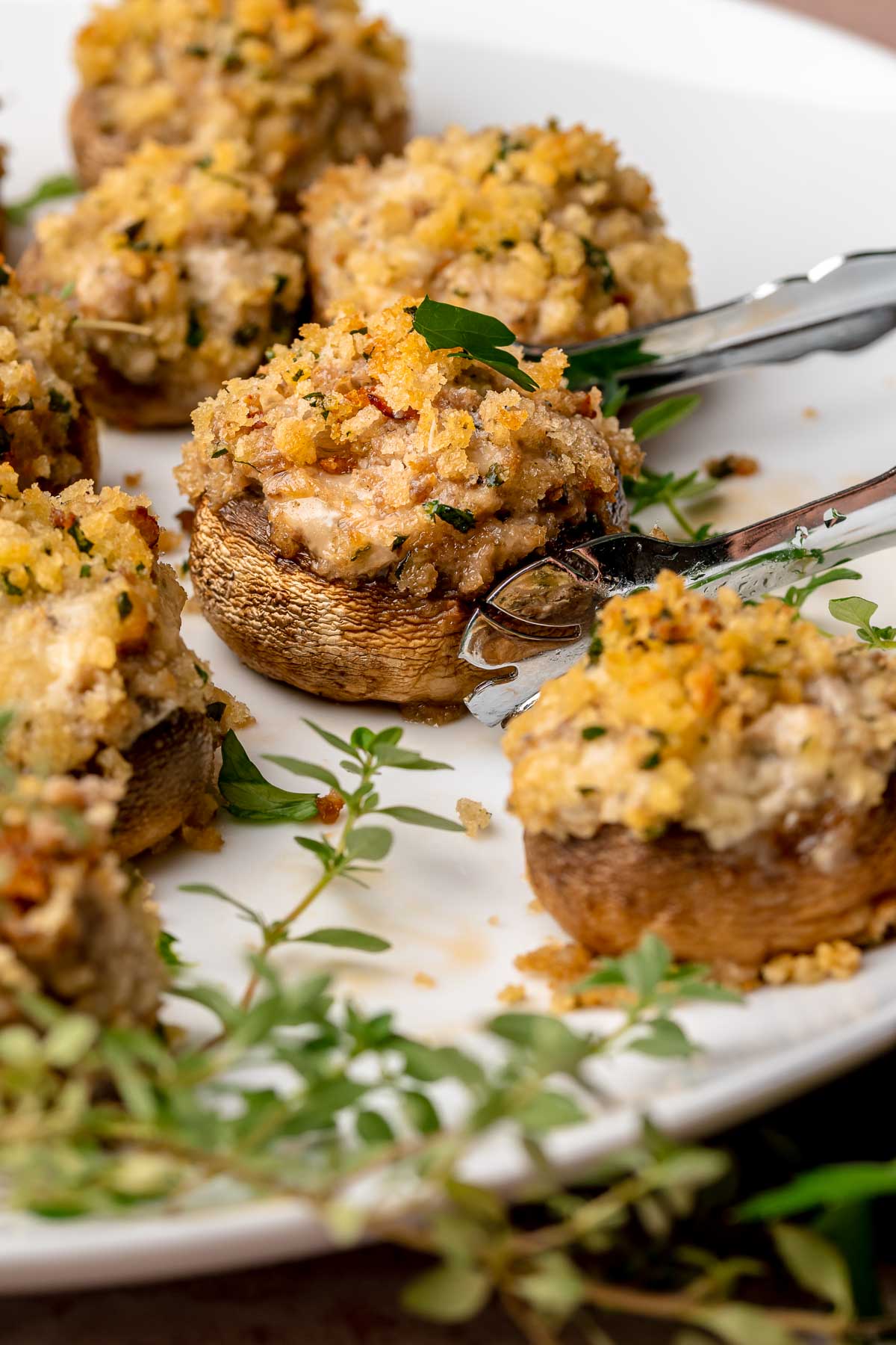 Tongs move around a boursin stuffed mushroom on a platter.