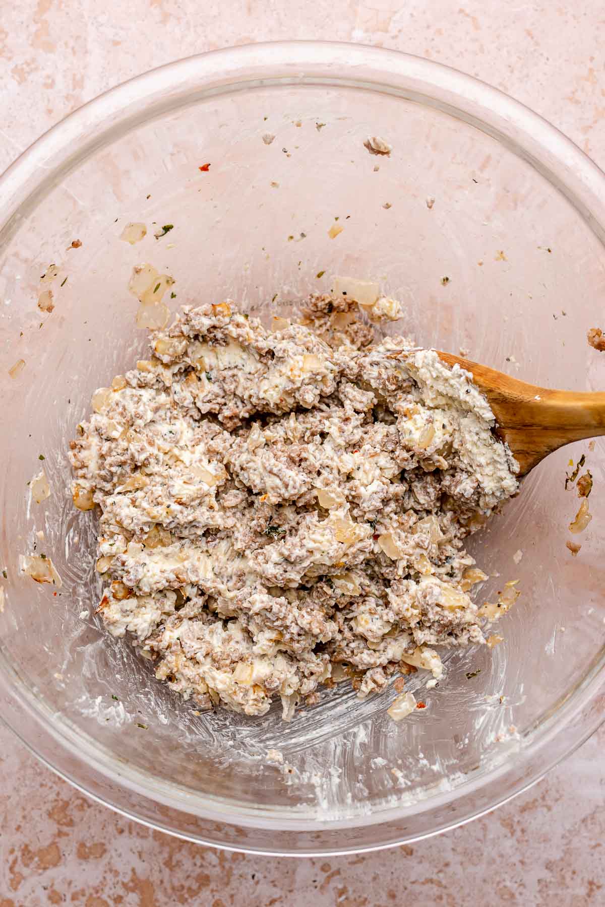 A wooden spoon mixes sausage and cheese filling in a bowl.