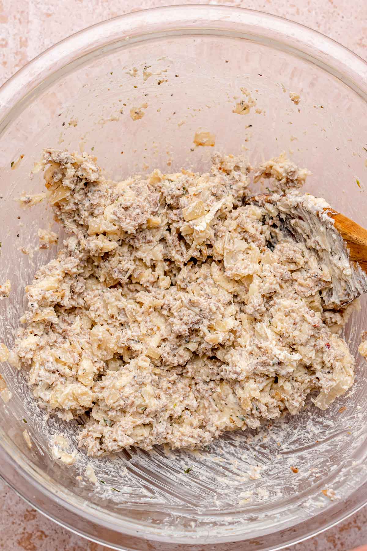 A wooden spoon mixes sausage and cheese filling in a bowl.