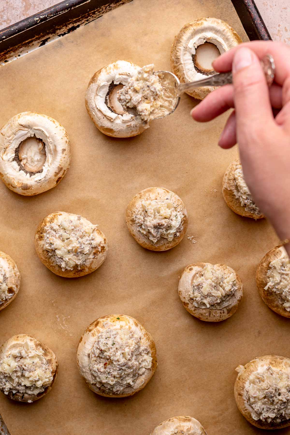 A spoons adds a dollop of sausage and cheese filling into mushroom caps.