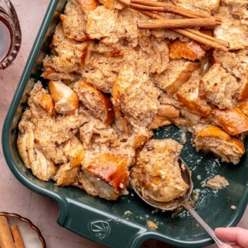 A hand scoops eggnog french toast casserole out of a dish.