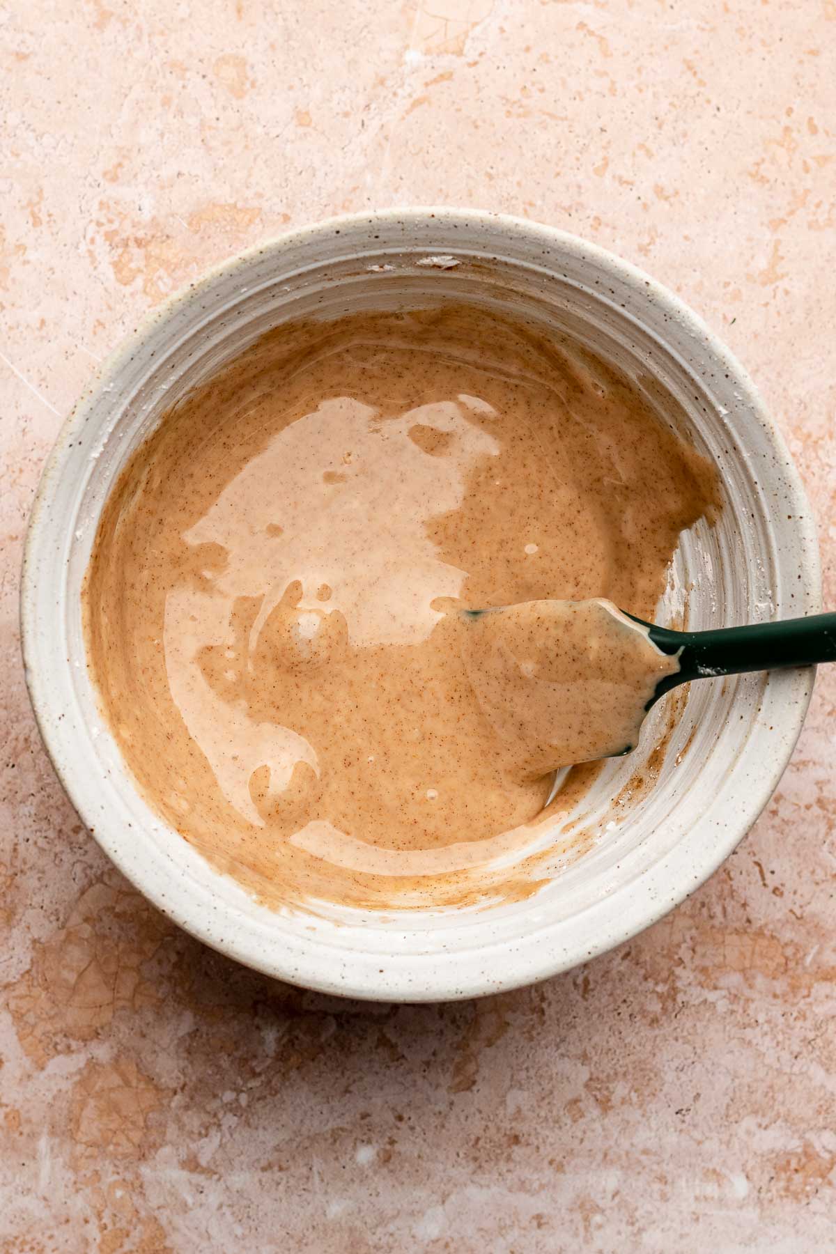 Cinnamon glaze in a bowl with a rubber spatula.