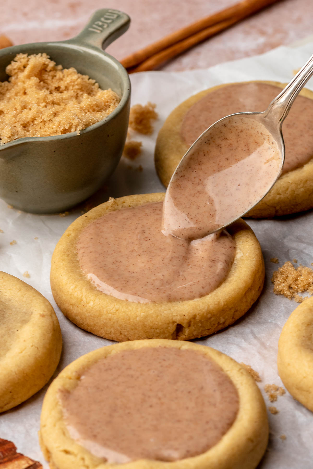 A spoon adds cinnamon glaze on top of baked cookies.
