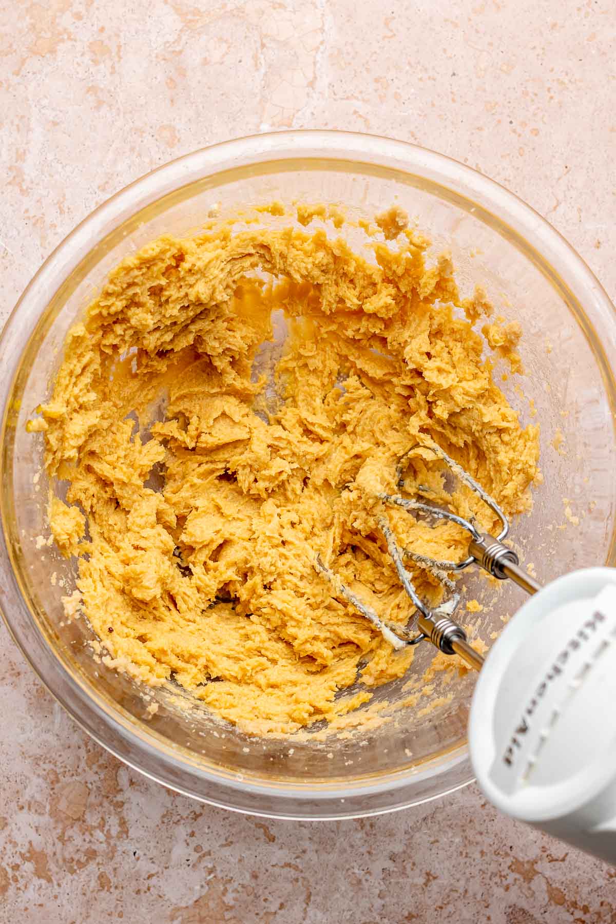 A hand mixer mixes cookie dough in a bowl.