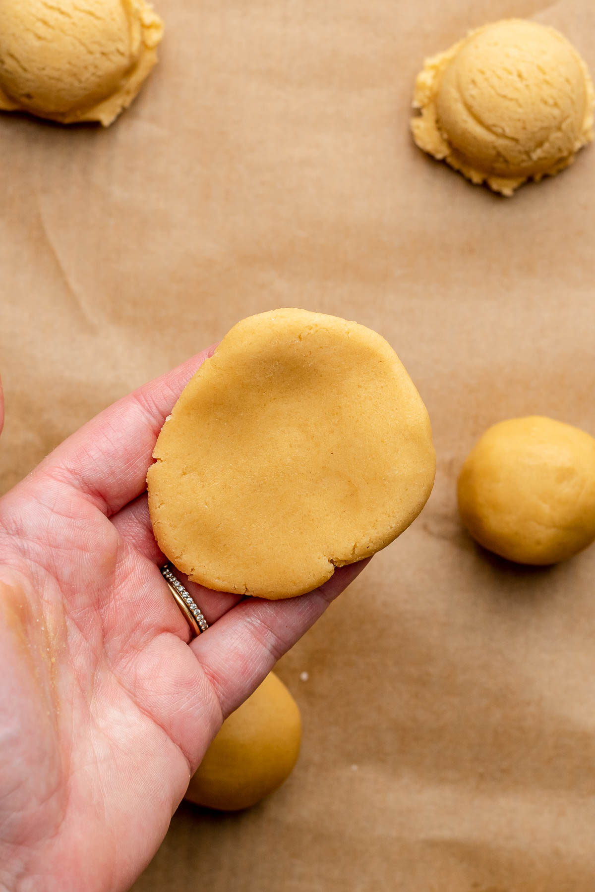 A hand holds a flattened piece of dough.