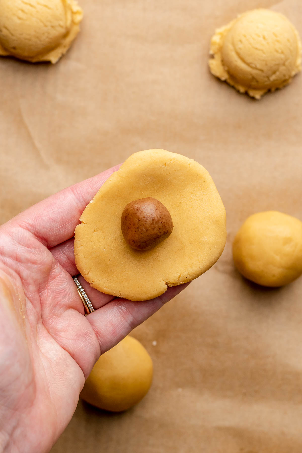A hand holds a piece of flattened dough with cinnamon sugar in the middle.
