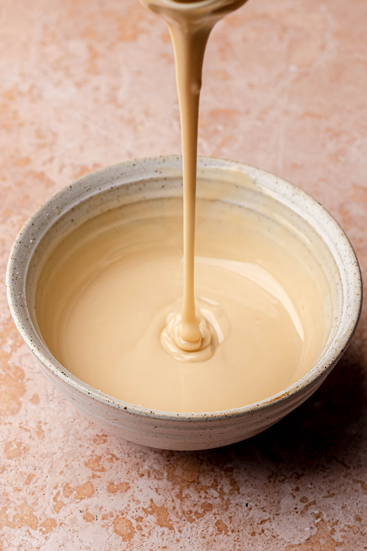 A whisk drizzles smooth maple glaze into a bowl.