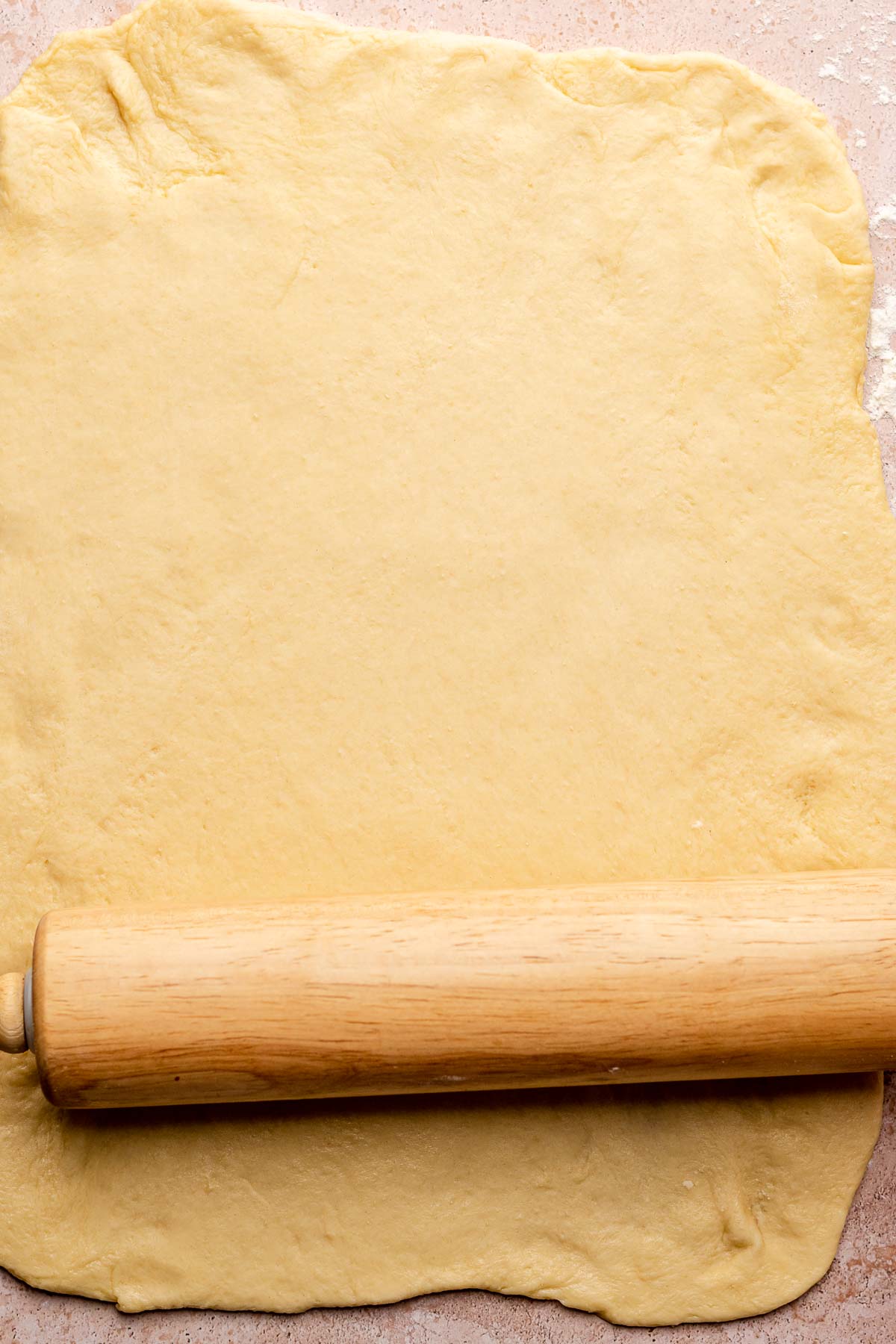 A rolling pin rolls dough into a rectangular sheet.