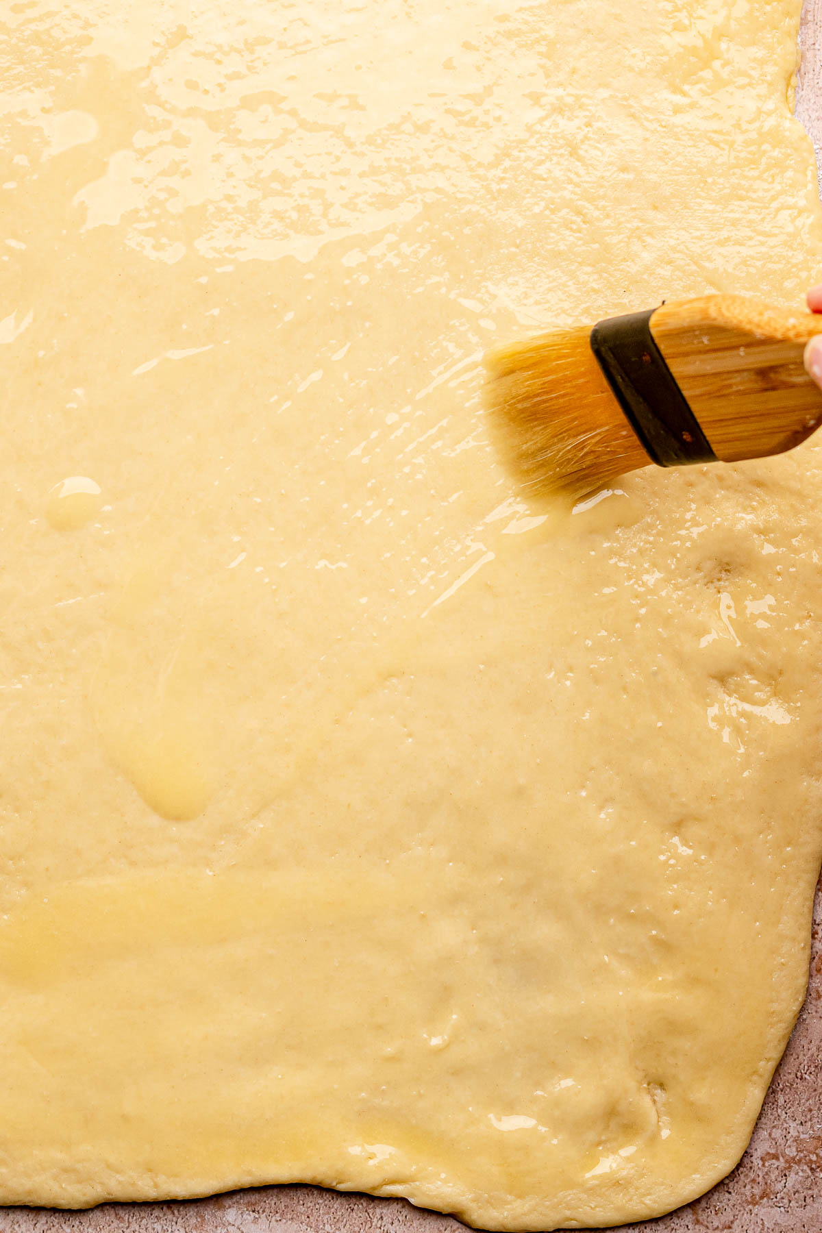 A pastry brush spreads melted butter onto rolled out dough.