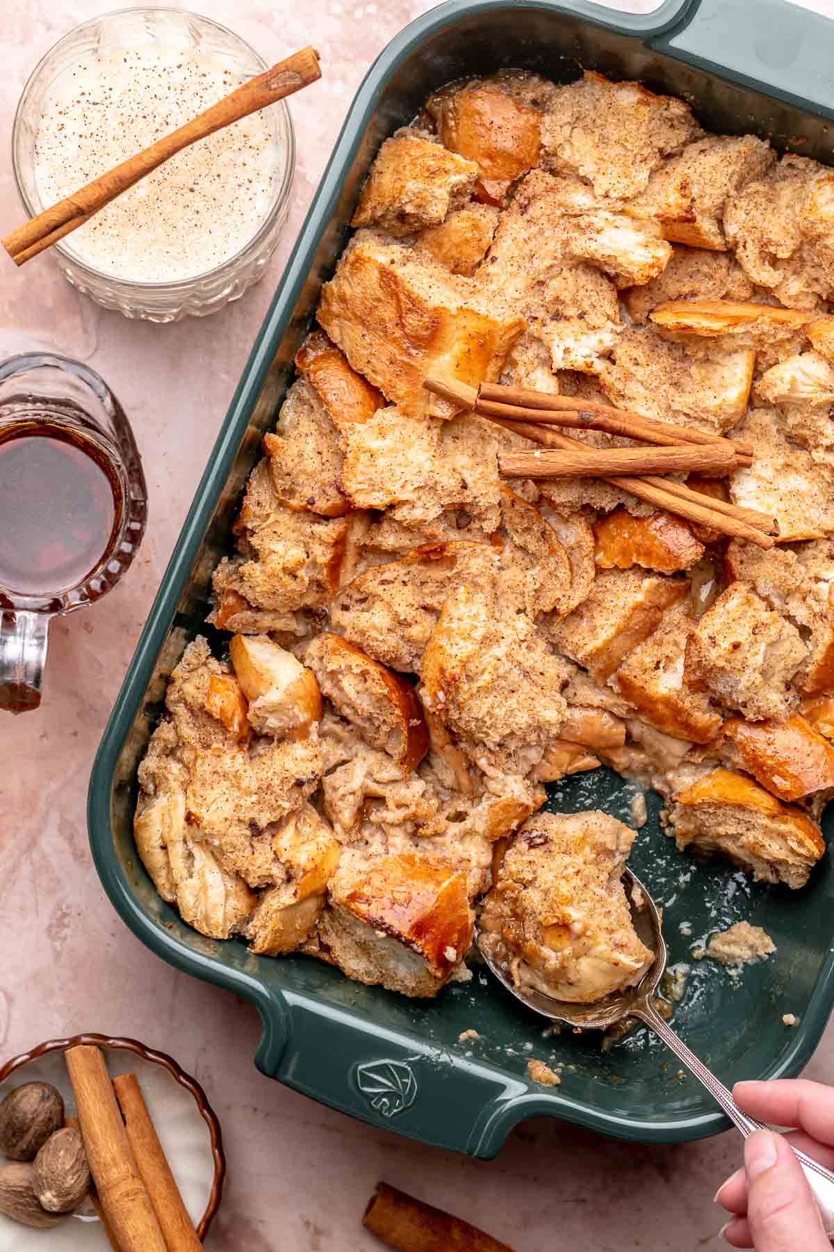 A hand scoops eggnog french toast casserole out of a dish.