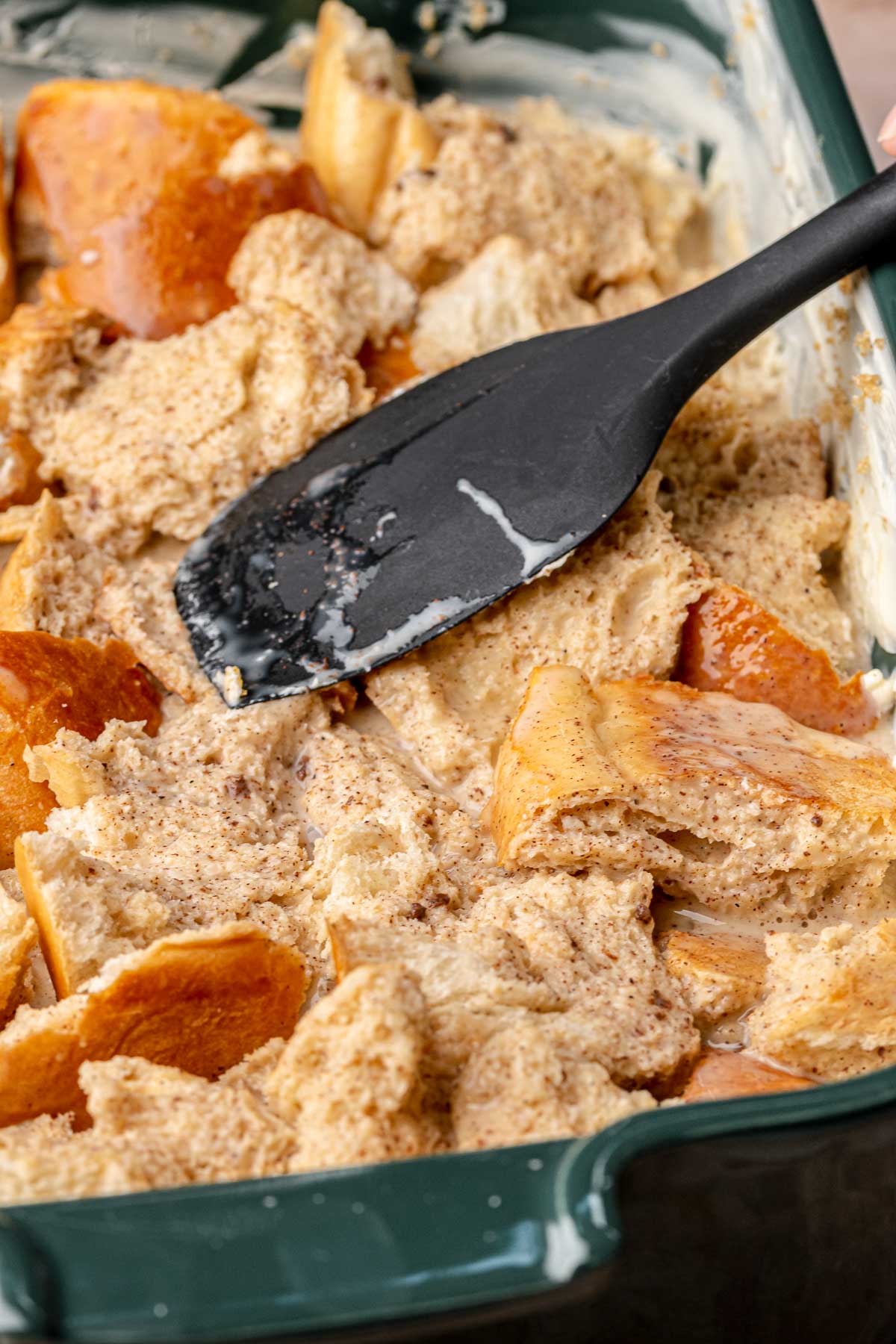 A spatula pushes the bread down into the custard.