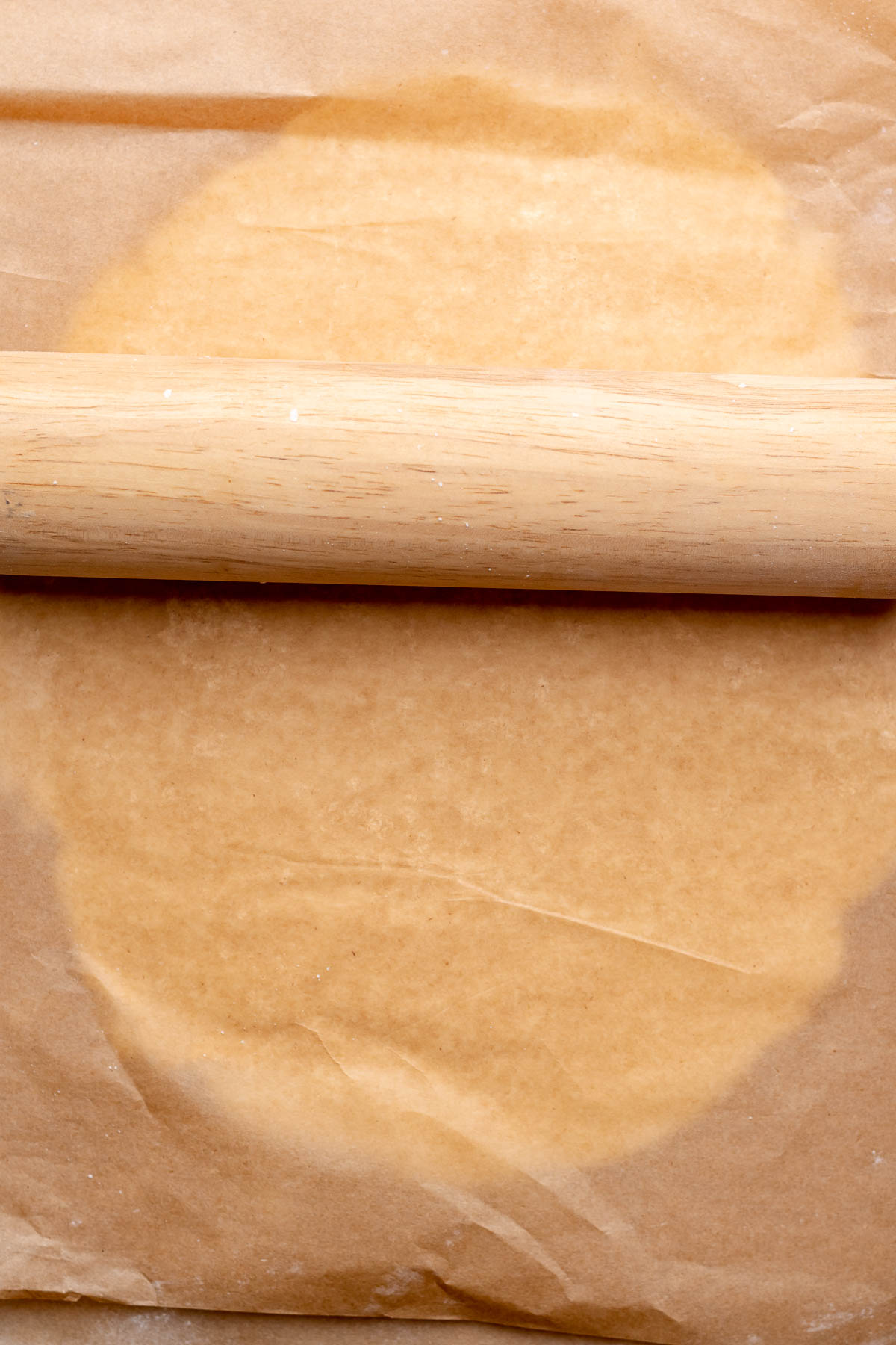 A rolling pin rolls out peppermint filling in between parchment paper.