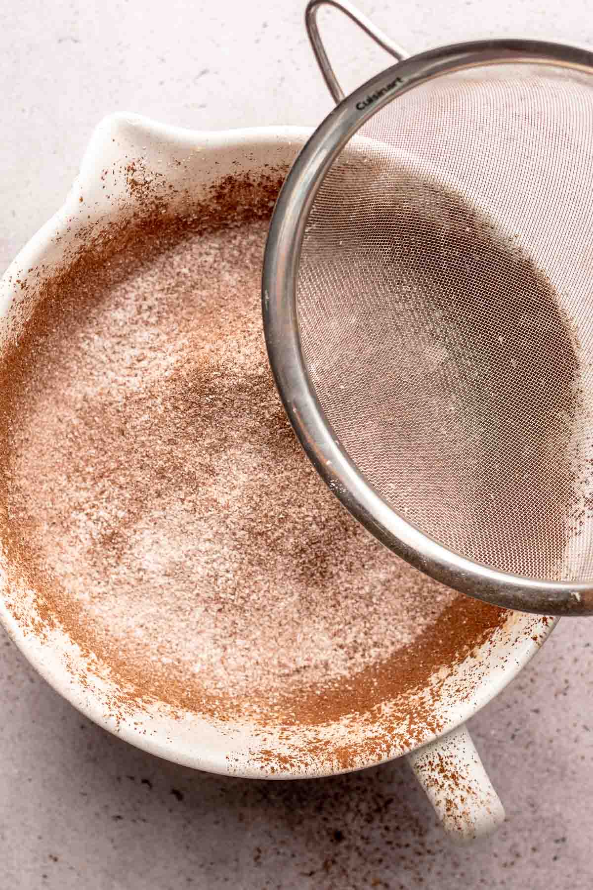 A fine mesh strainer sifts dry ingredients into a bowl.