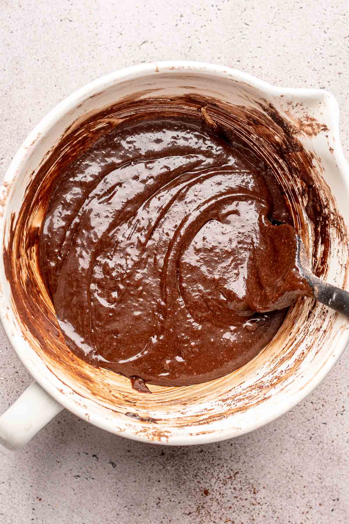 A rubber spatula mixes brownie batter in a bowl.