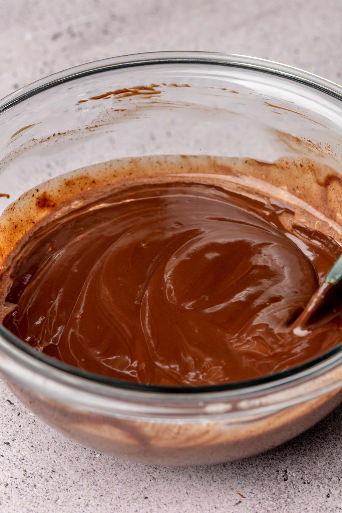A spatula mixes chocolate ganache in a bowl.