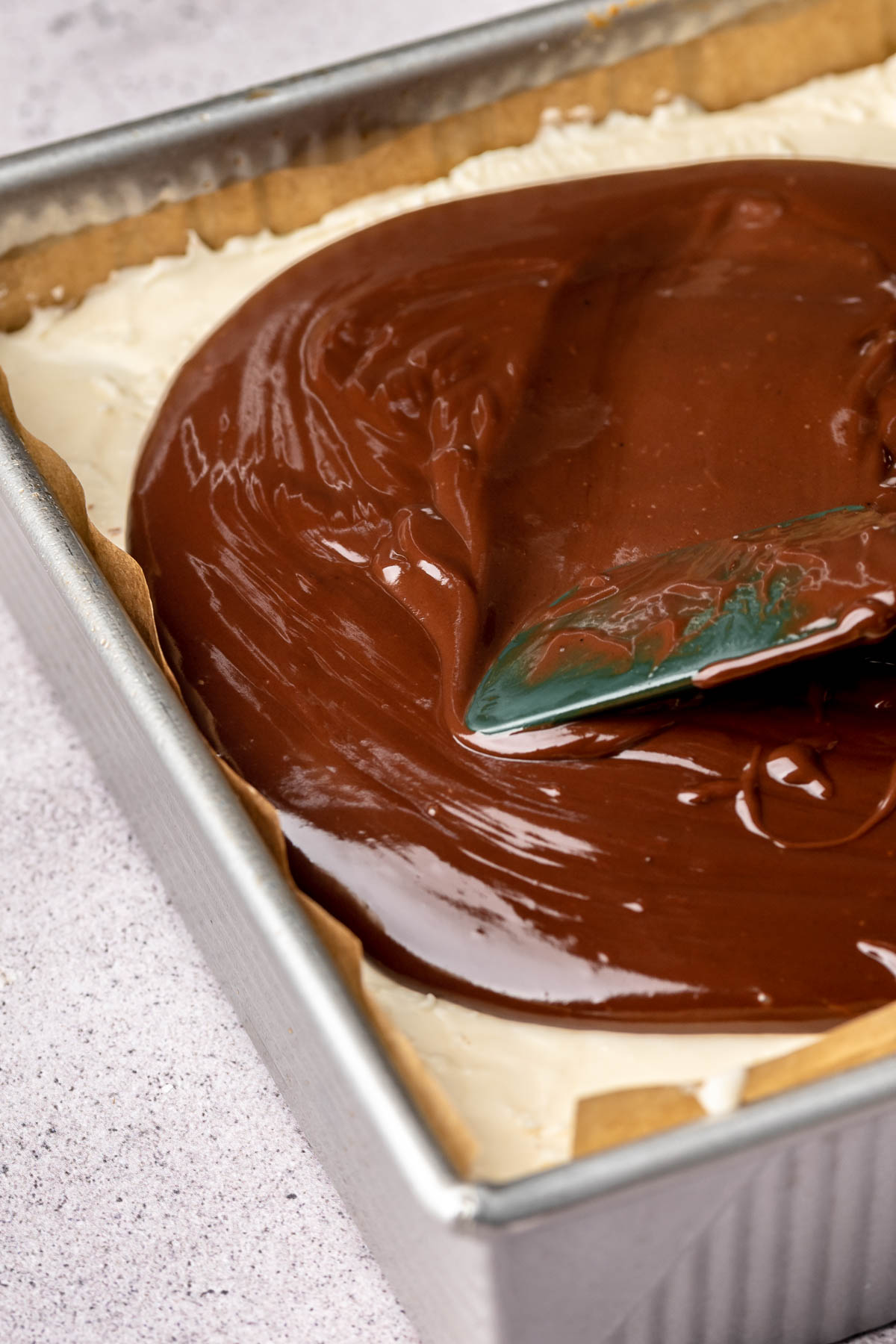 A spatula spreads chocolate ganache onto brownies.