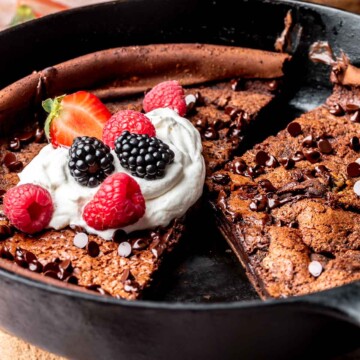 Sliced chocolate dutch baby in a pan with whipped cream and berries.