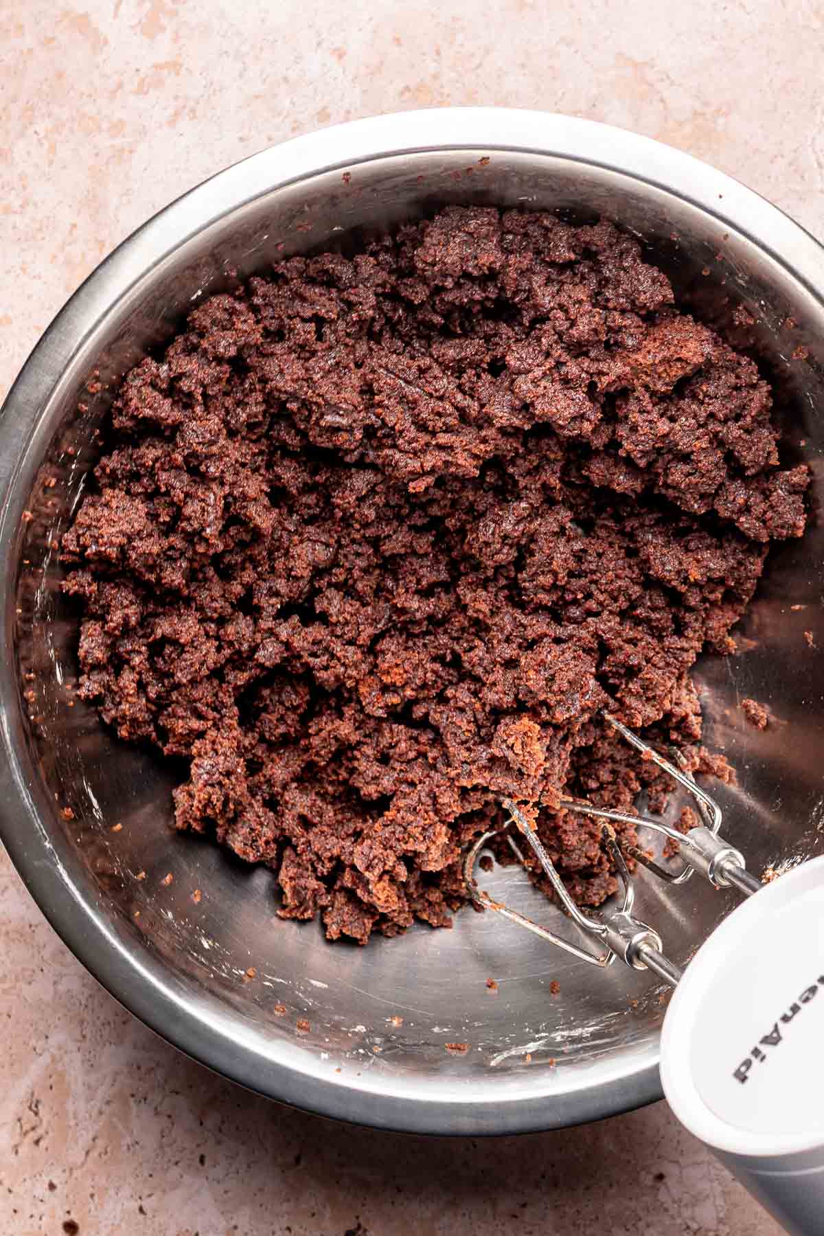 A hand mixer mixes brownies and cream cheese in a bowl.