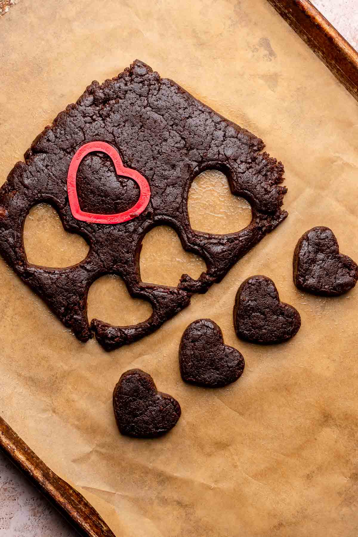 A heart cookie cutter cuts brownies into heart shapes on parchment paper.