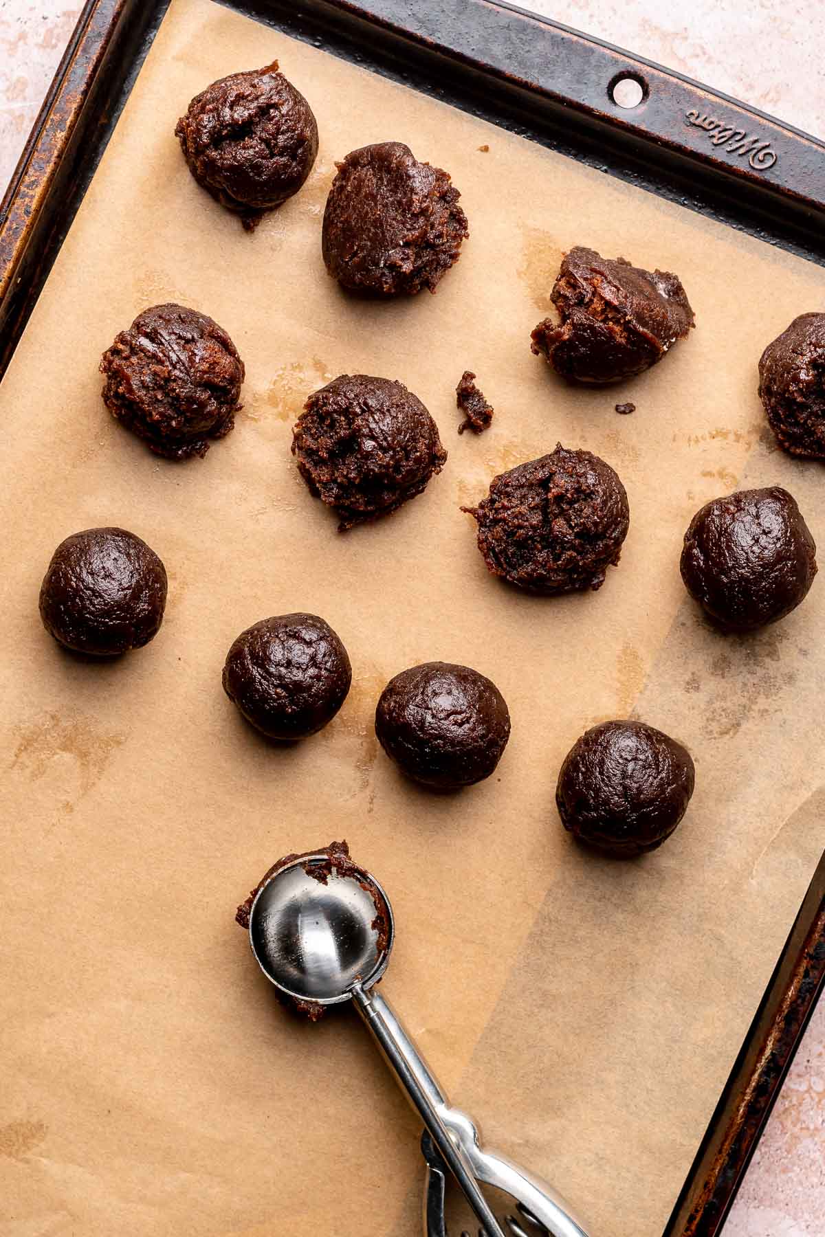 A cookie scoop next to balls of brownie truffles on a pan.