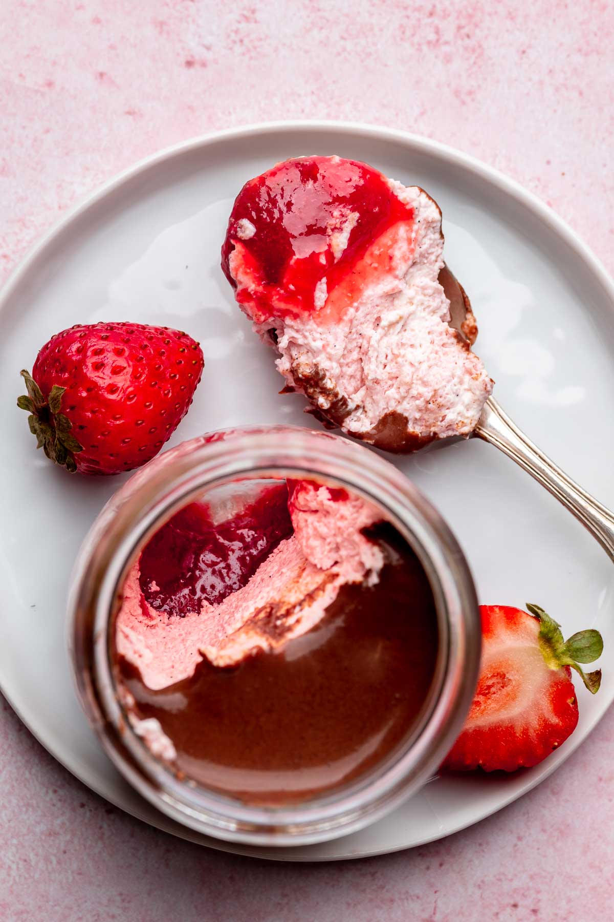 Chocolate strawberry mousse in a glass jar with a bite removed sitting on a spoon.