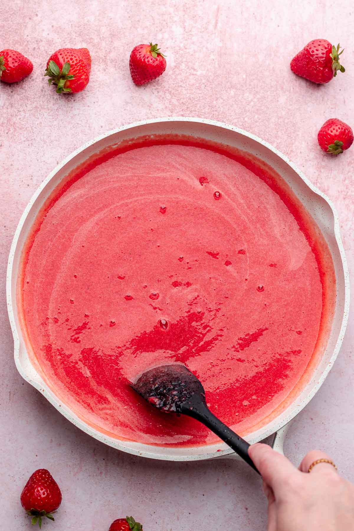A spatula stirs strawberry puree in a pan.