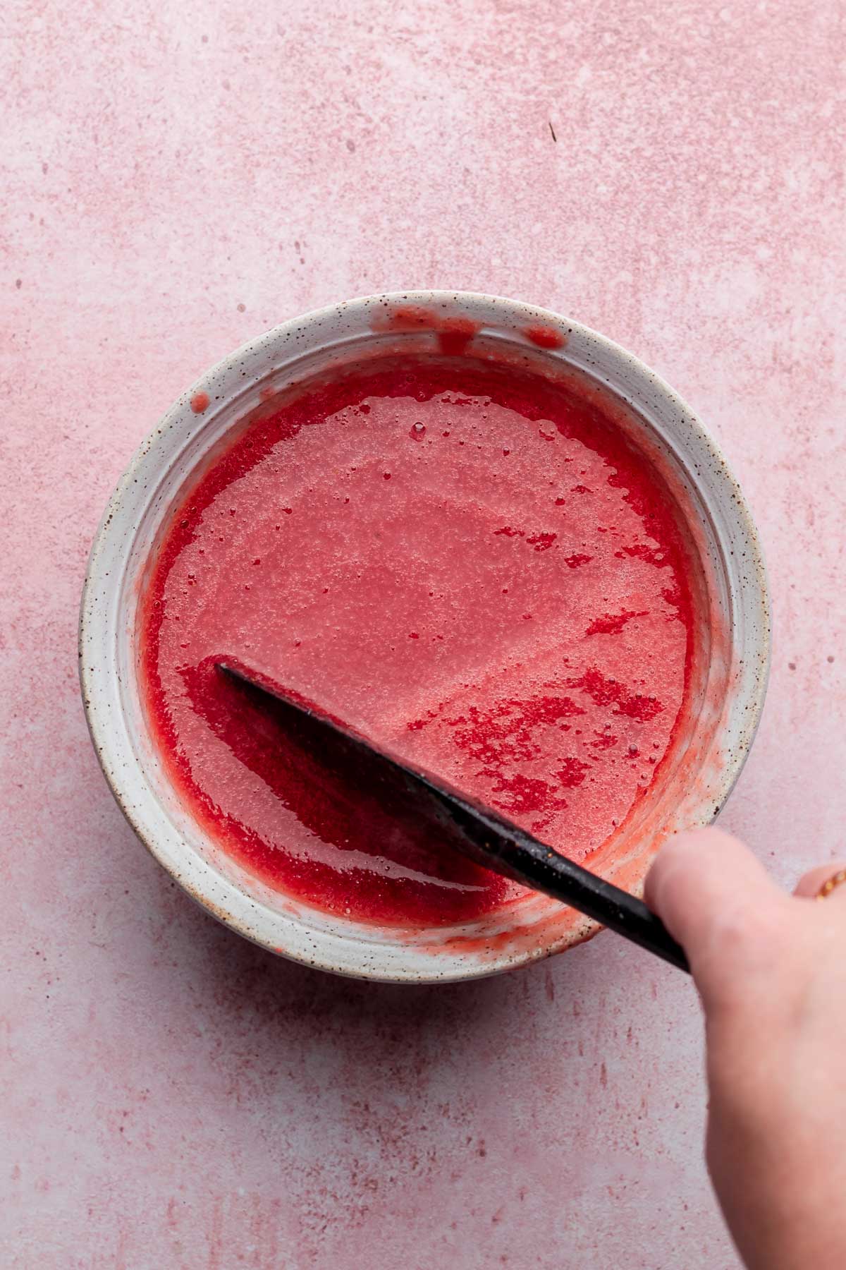 A spatula stirs a bowl of strawberry puree.