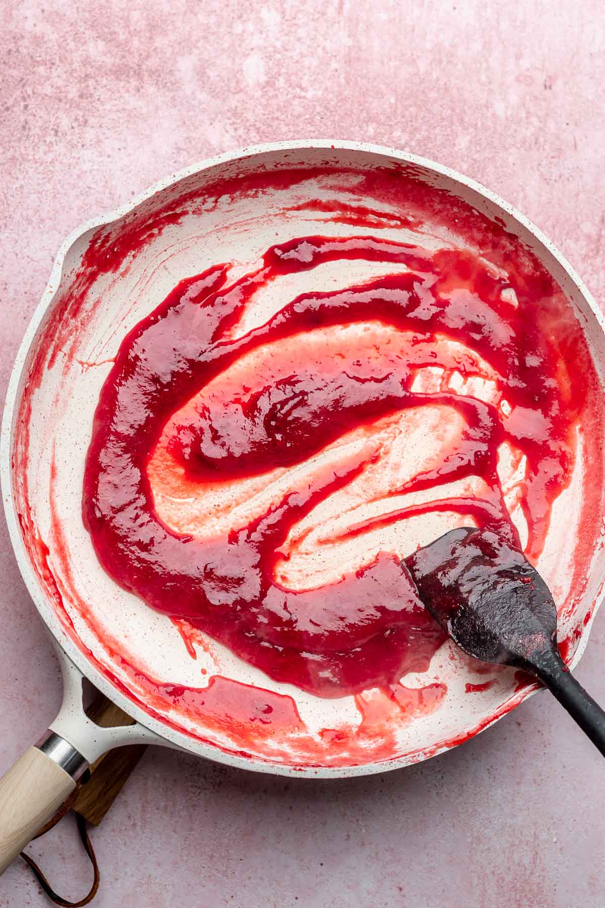 A spatula swipes through cooked down strawberry puree in a pan.