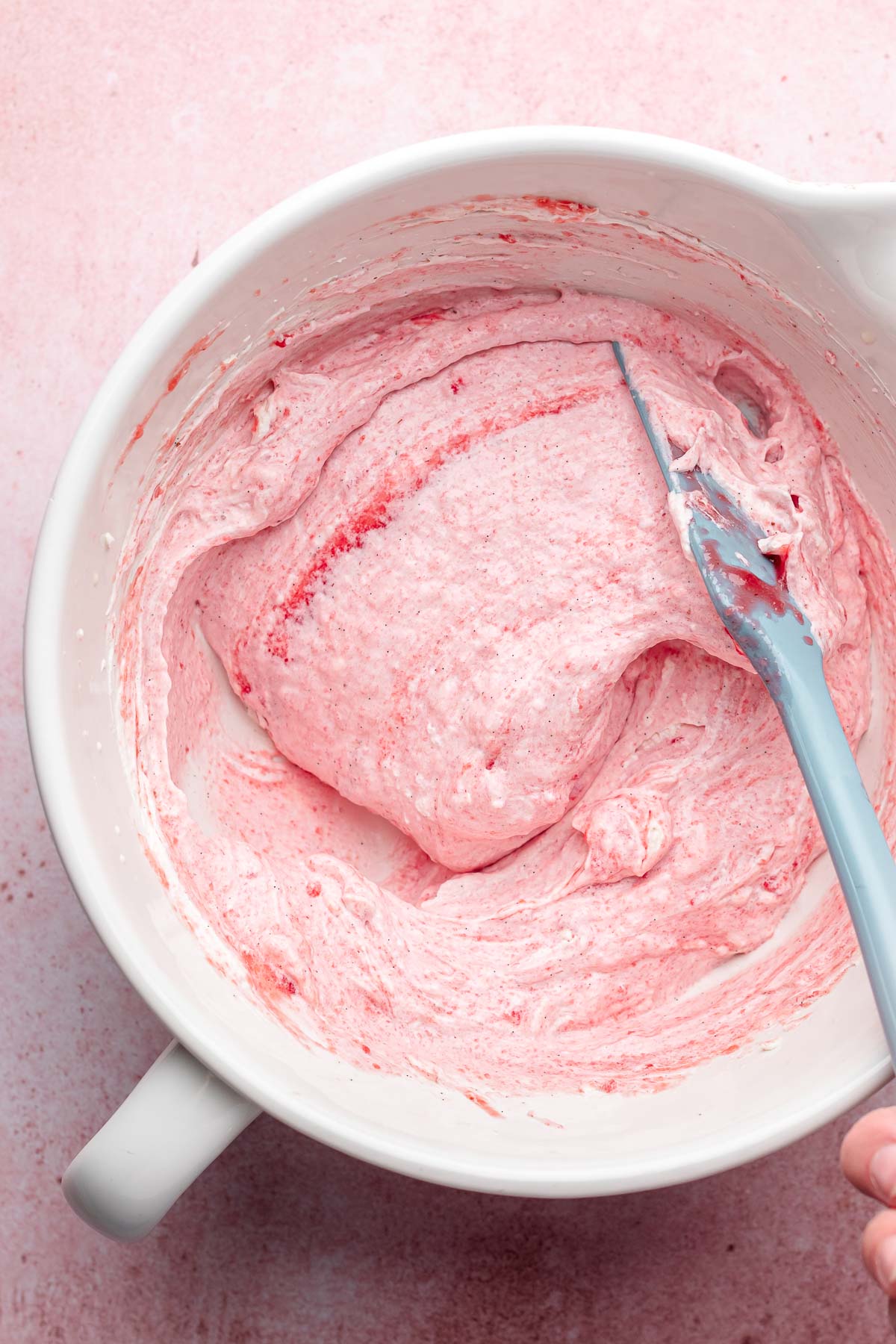 A spatula folds together strawberry mousse in a bowl.