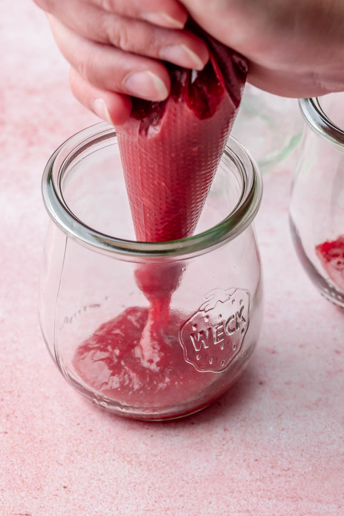 A piping bag adds strawberry puree to the bottom of a glass jar.