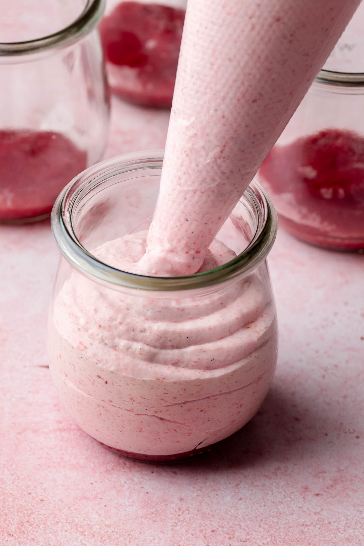 A piping bag adds strawberry mousse to a glass jar.