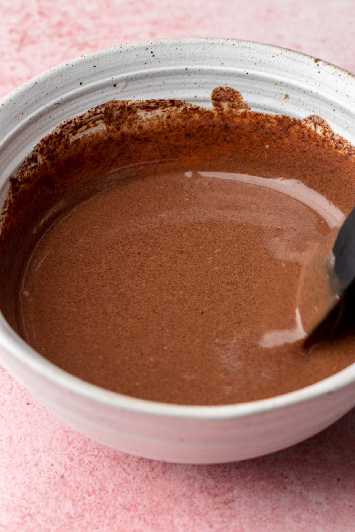 A spatula mixes chocolate ganahce in a bowl.
