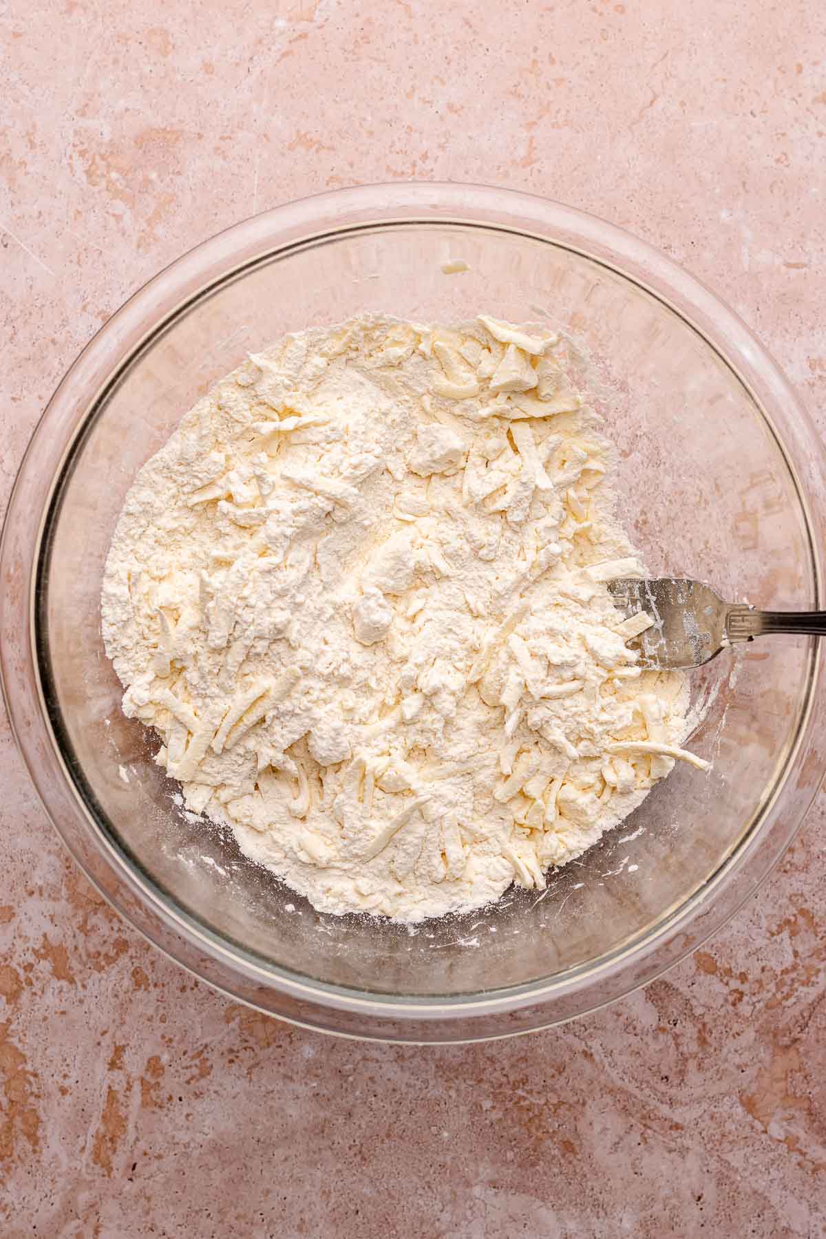 A fork mixes dry ingredients and shredded butter in a bowl.