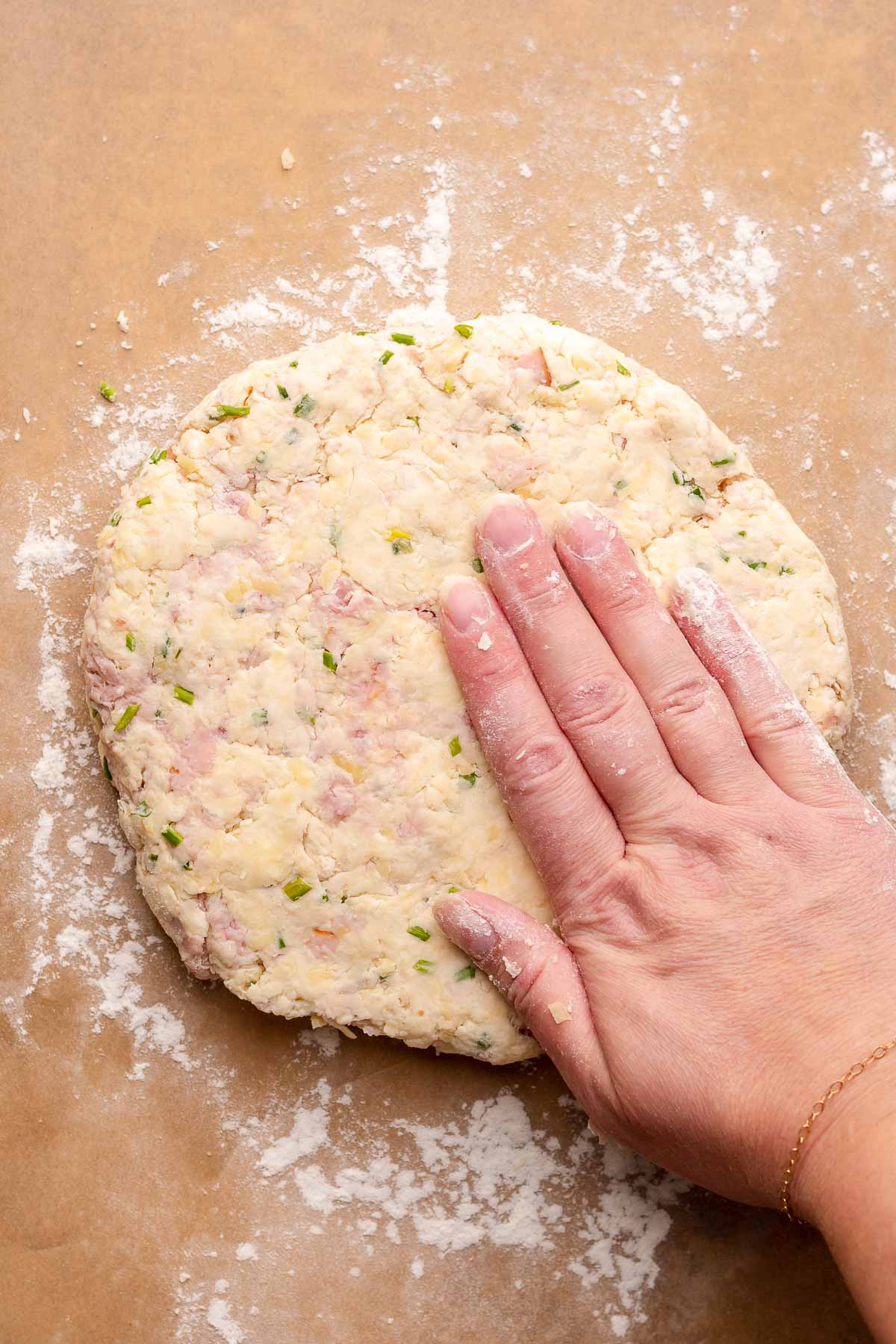 A hand pats scone dough into a circle on a piece of parchment paper.