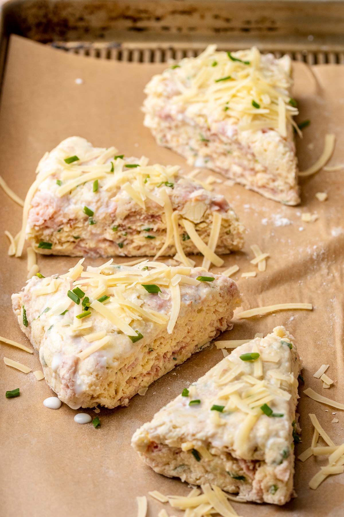 Ham and cheese scones topped with cheese and chives before baking.